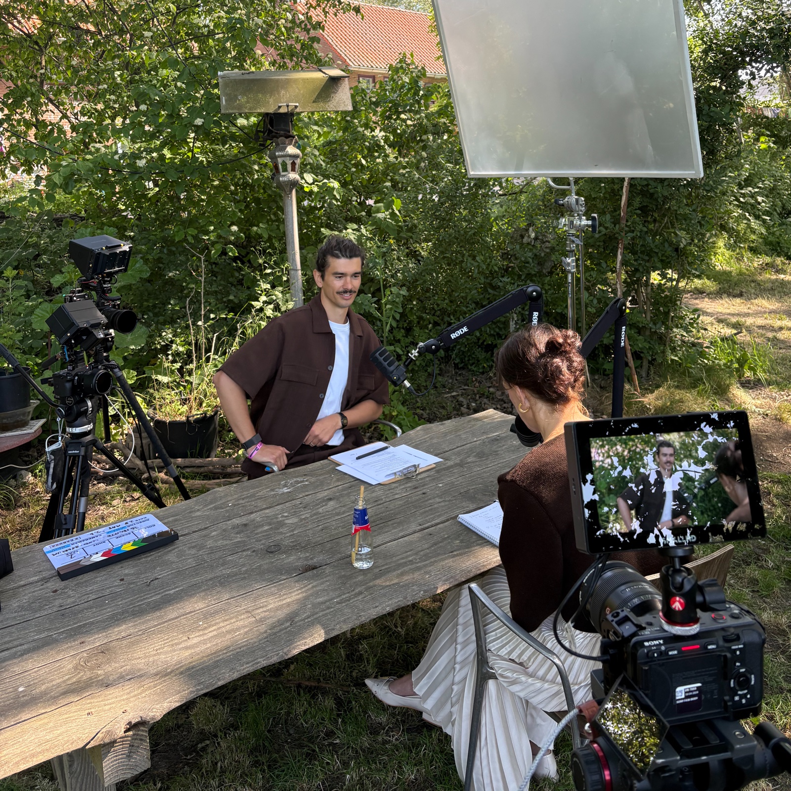 Kyle interviewing a founder outdoors at a wooden table, boom mics in frame
