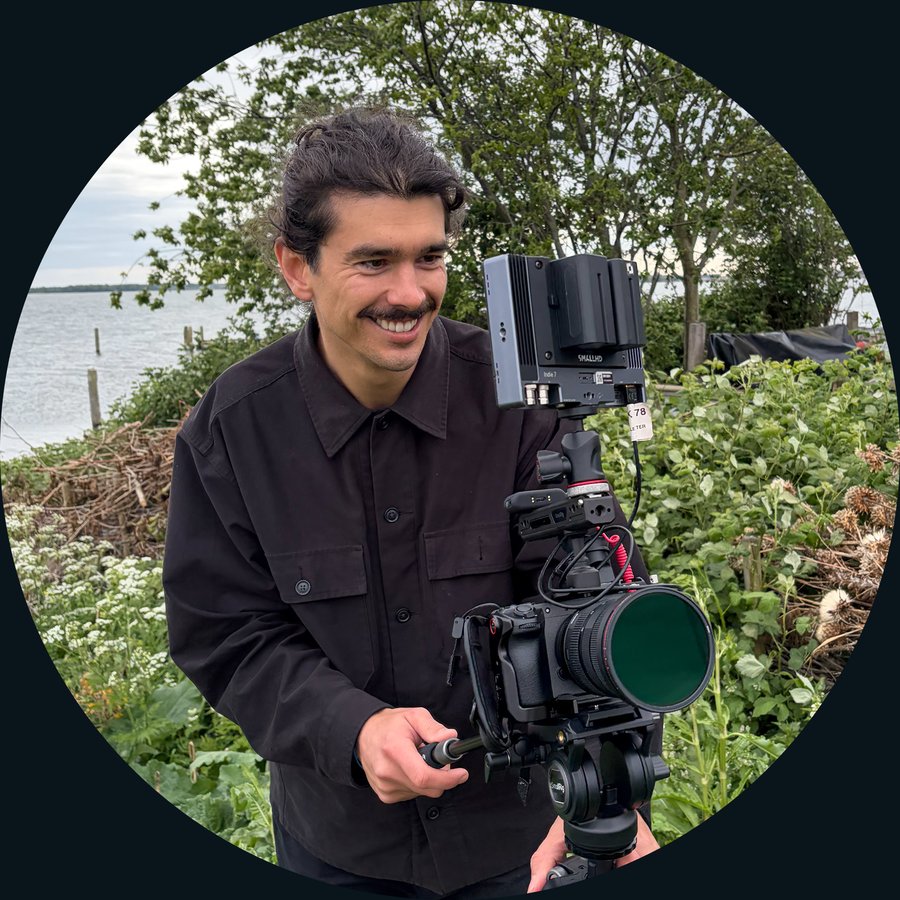 Portrait of Kyle Oberholzer holding a camera on a tripod by the water